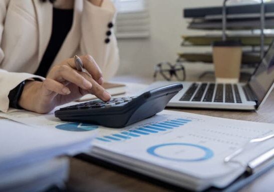 Person using calculator amid financial charts and laptop.